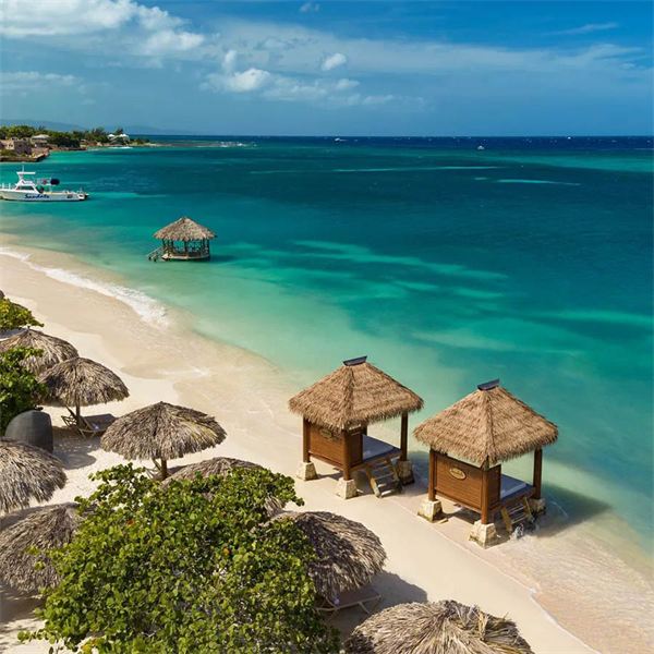 Thatched cabanas on a white sand beach beside turquoise Caribbean water, seen from above.